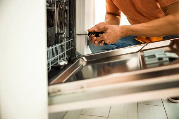 Close-up of a technician using a screwdriver to adjust the door hinge of a stainless steel dishwasher.