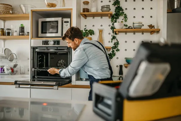 Expert technician using a screwdriver to repair the internal heating element of a modern white electric oven